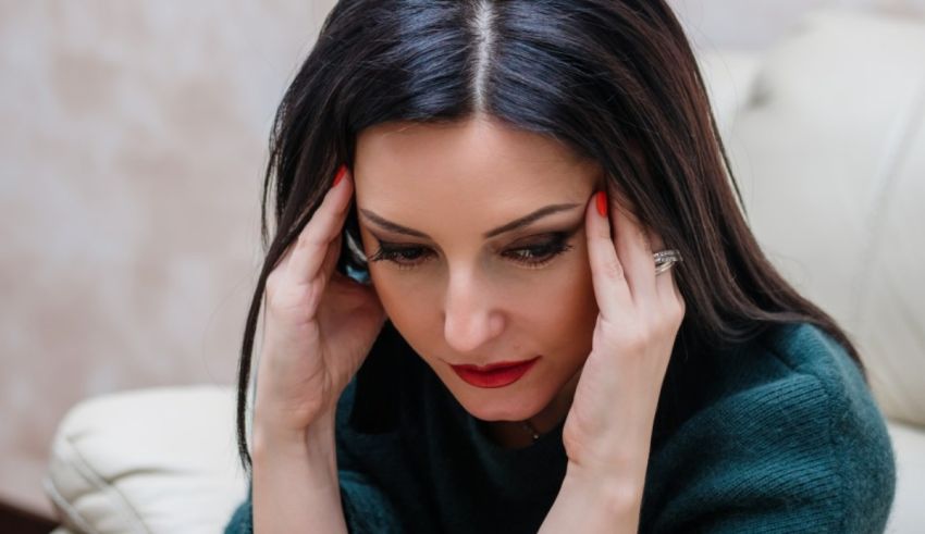 A woman is holding her head while sitting on a couch.