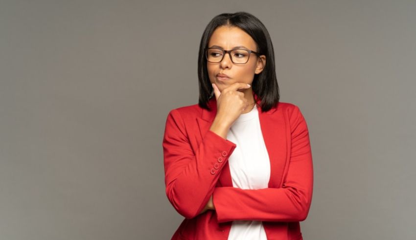 A young business woman in a red blazer posing with her hands on her hips.