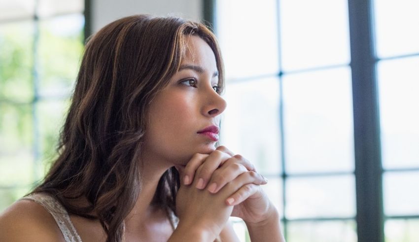 A woman looking at the window with her hand on her chin.