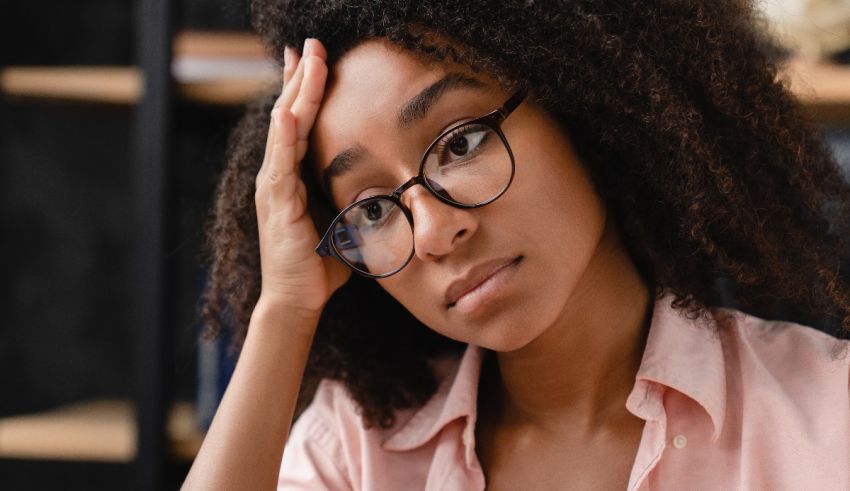 A black woman with glasses is holding her head in her hands.