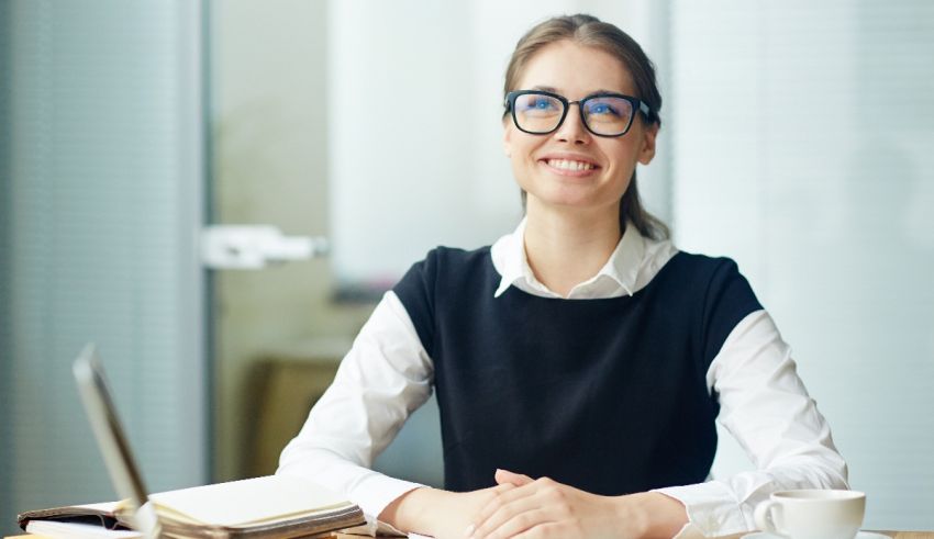 A woman in glasses sitting at a desk with a cup of coffee.
