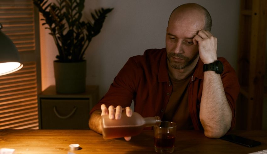 A bald man sitting at a table with a bottle of alcohol.