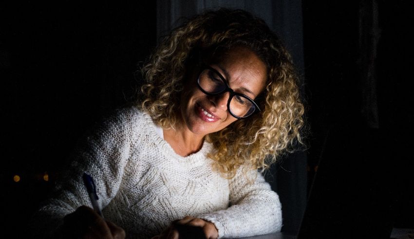 A woman in glasses writing on a laptop at night.