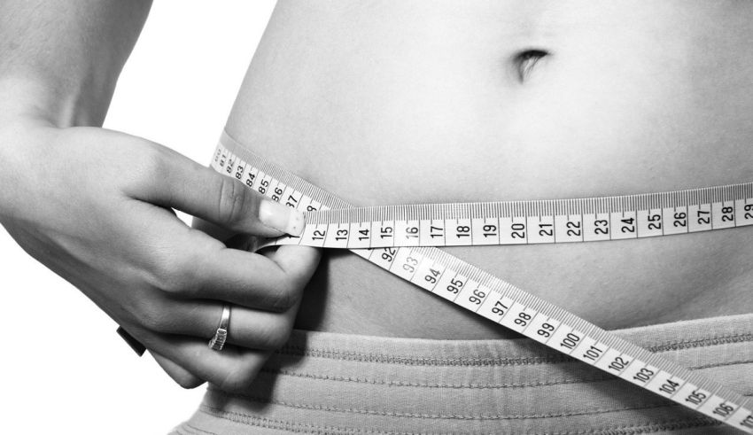 A woman is measuring her waist with a measuring tape.