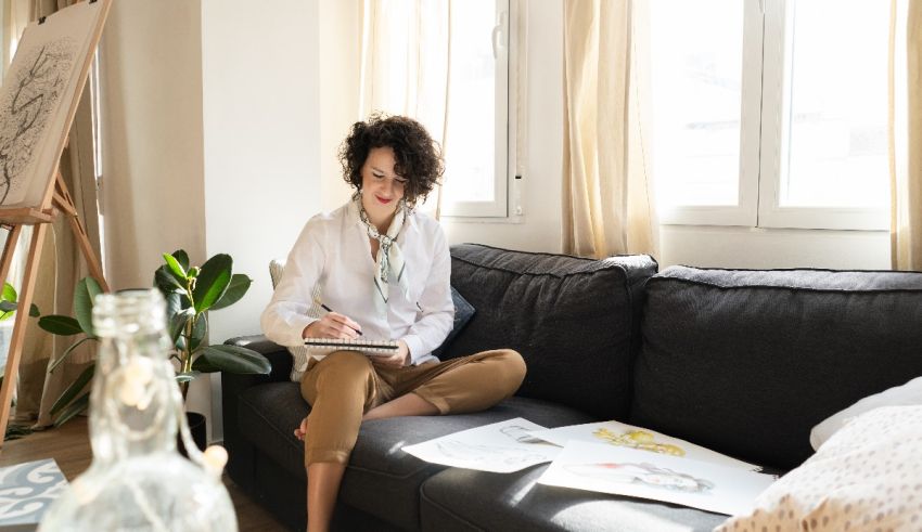 A woman sits on a couch and writes in a notebook.