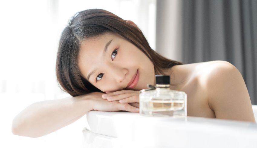 A young asian woman laying in a bathtub with a bottle of perfume.