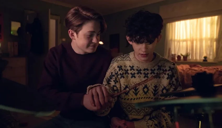 Two boys are sitting in a room with a drum set.