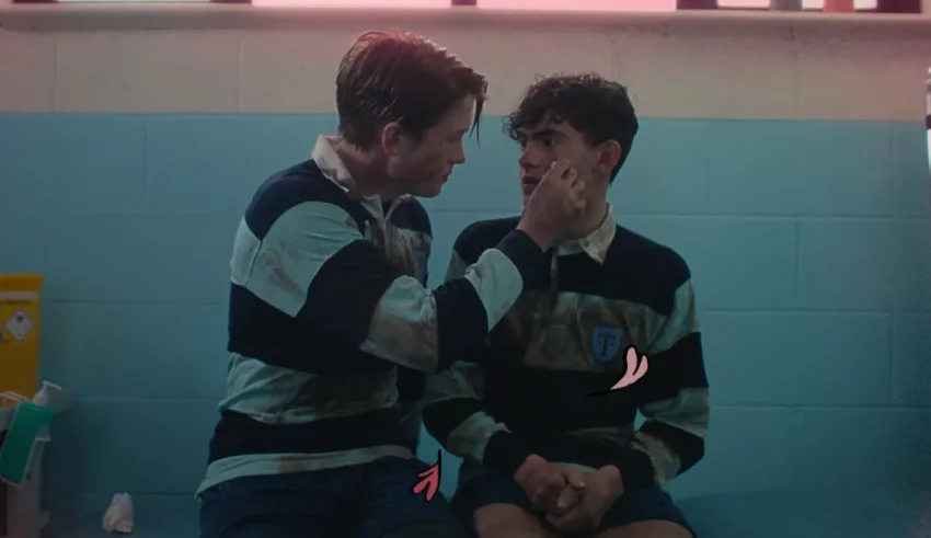 Two boys sitting in a locker room talking to each other.