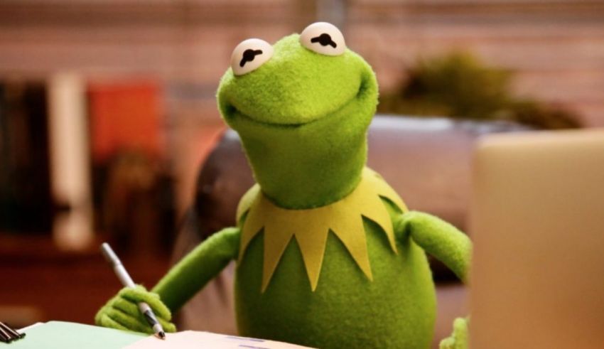 A green frog sitting at a desk with a pen.