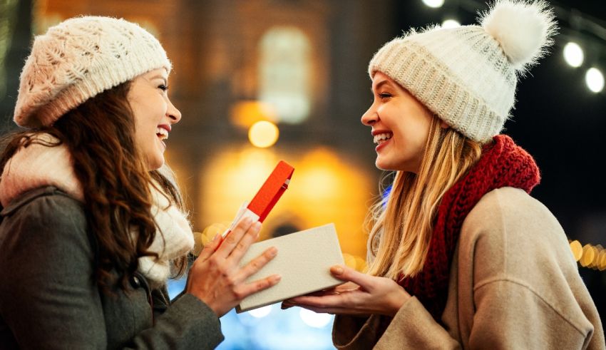 Two women holding a gift box in front of a christmas tree.
