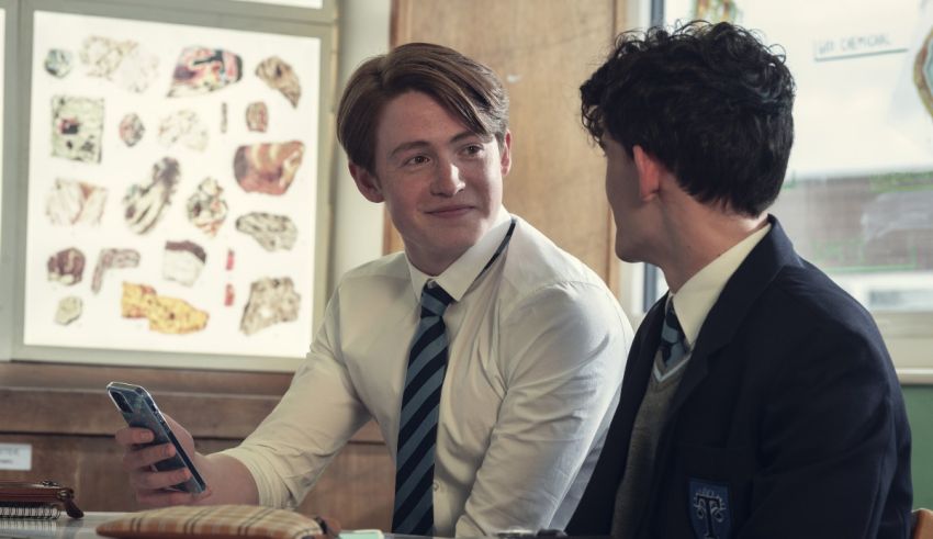 Two young men sitting at a table looking at a cell phone.