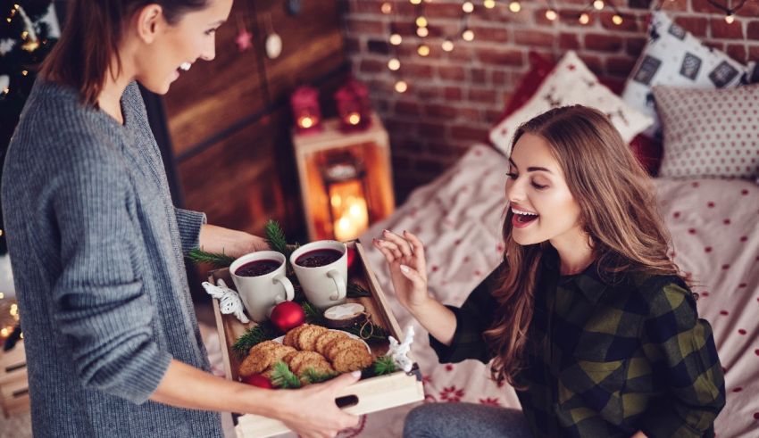 A woman is holding a tray of coffee and cookies in front of a christmas tree.