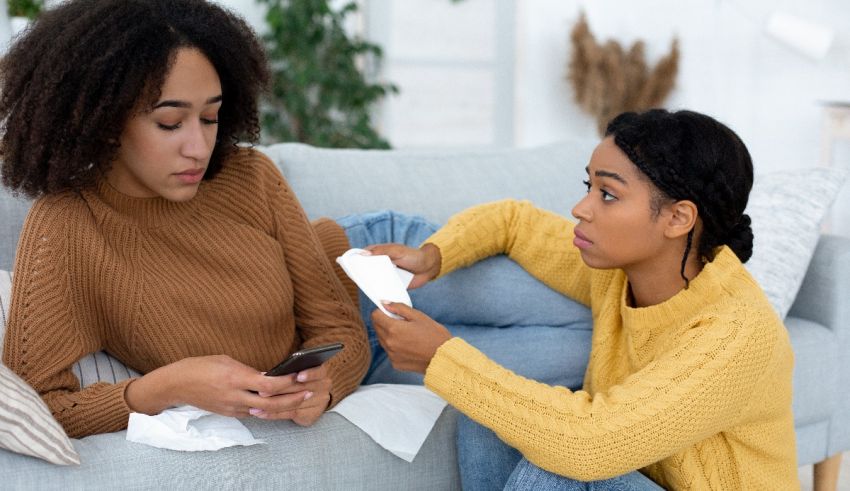 Two women sitting on a couch with a cell phone.