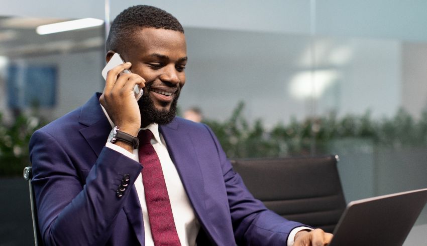 A businessman in a suit talking on the phone while working on a laptop.
