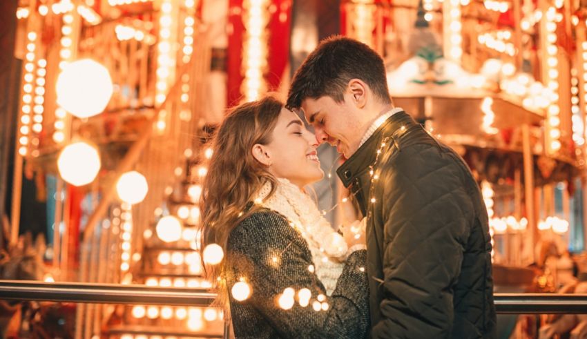 A couple kisses in front of a carousel.