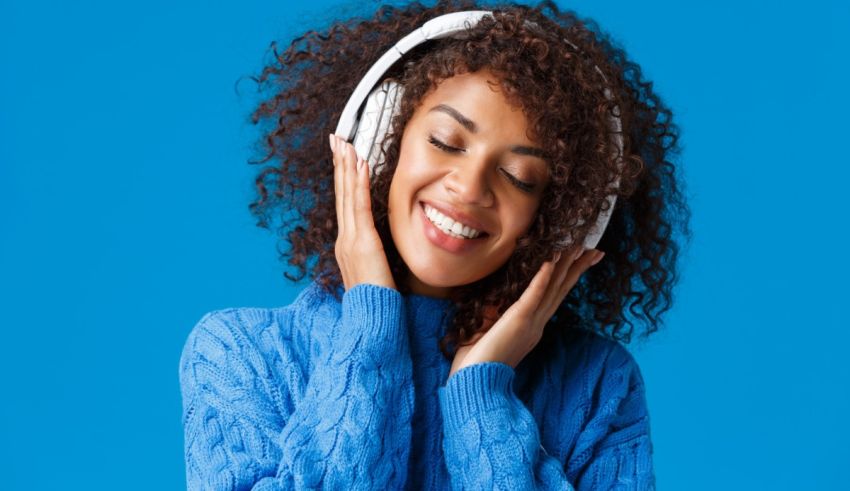 Young woman listening to music with headphones on blue background.