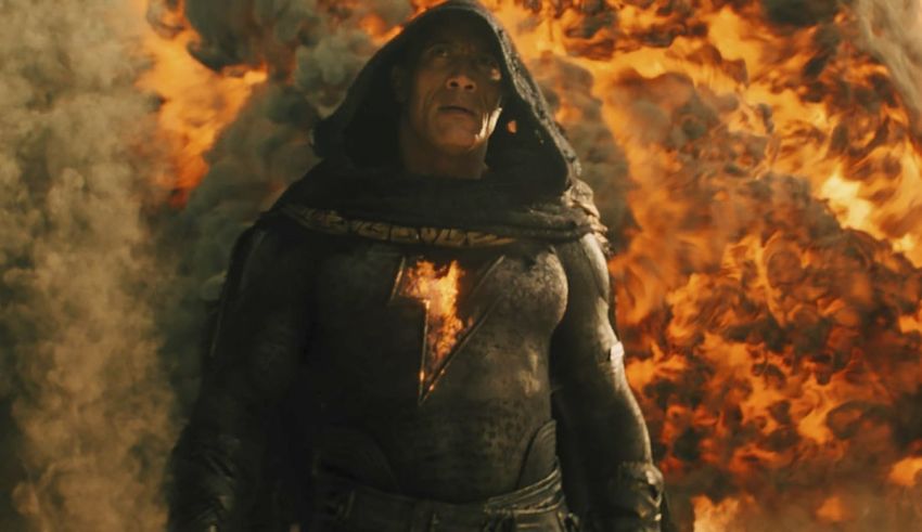 A man in a cloak standing in front of a fire.