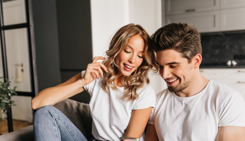 A young man and woman are sitting on a couch and using a cell phone.