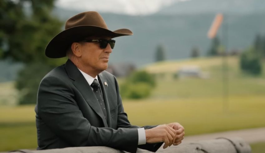 A man in a suit and hat sitting on a fence.