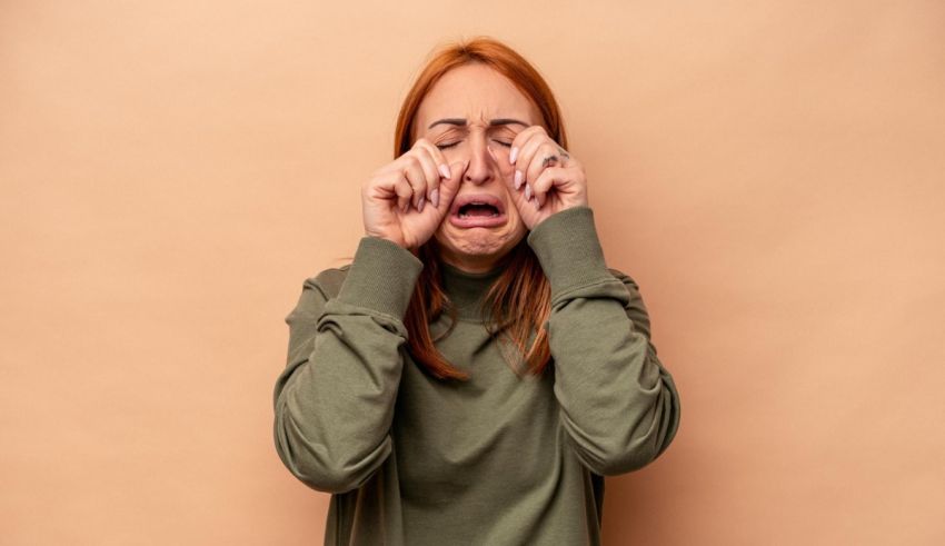 A woman covering her eyes with her hands on a beige background.