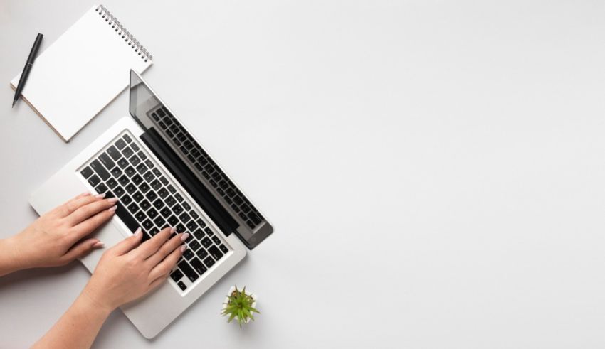 A woman typing on a laptop on a white table.