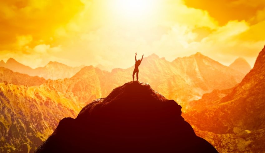 A man standing on top of a mountain with his arms raised in the air.