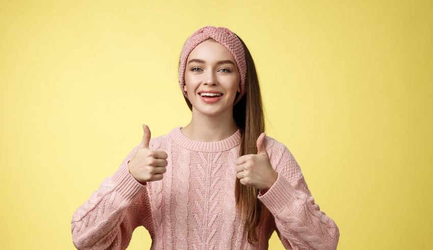 Young woman giving thumbs up on yellow background.