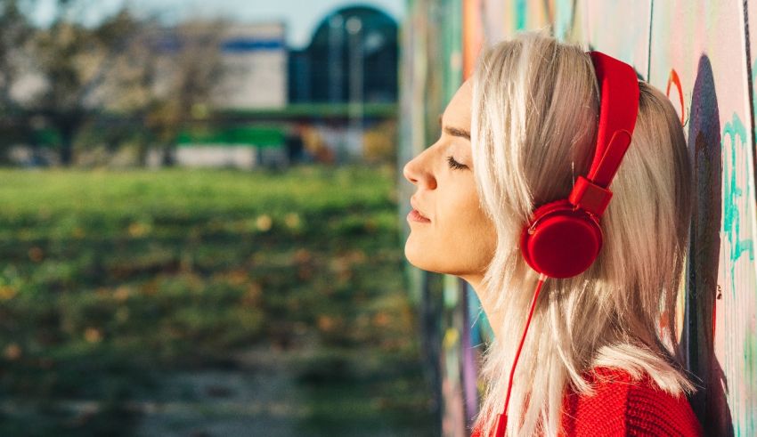 A woman wearing red headphones leaning against a graffiti wall.