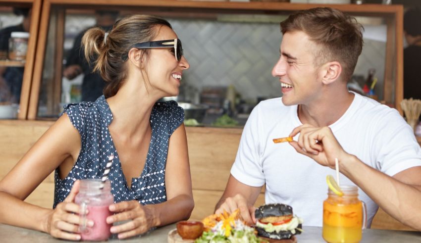 A man and woman sitting at a table with food and drinks.
