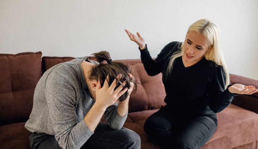 A woman is sitting on a couch with her hands on her head.