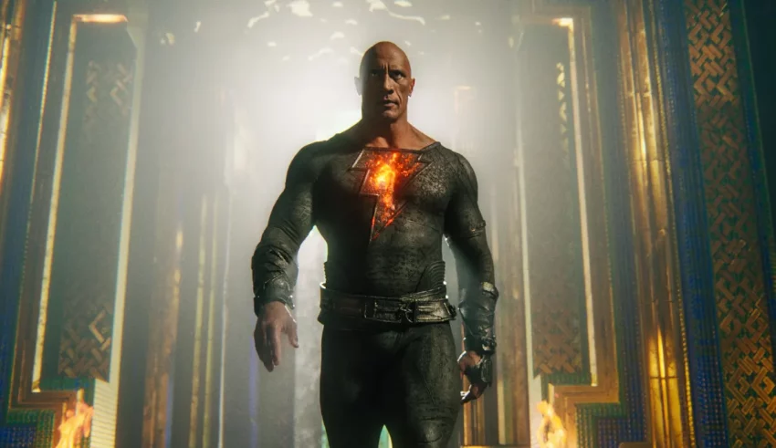 A man in a black suit standing in a dark hallway.