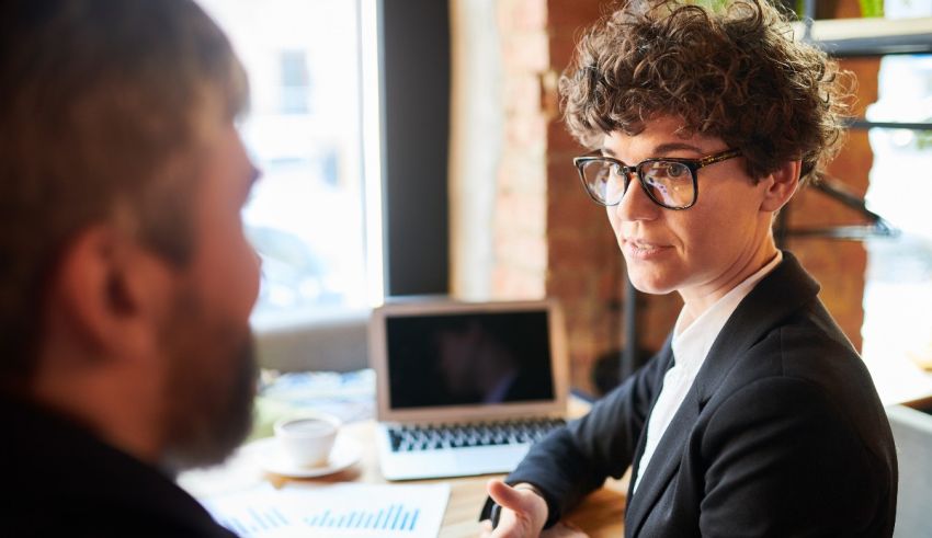 A woman in glasses is talking to a man at a table.