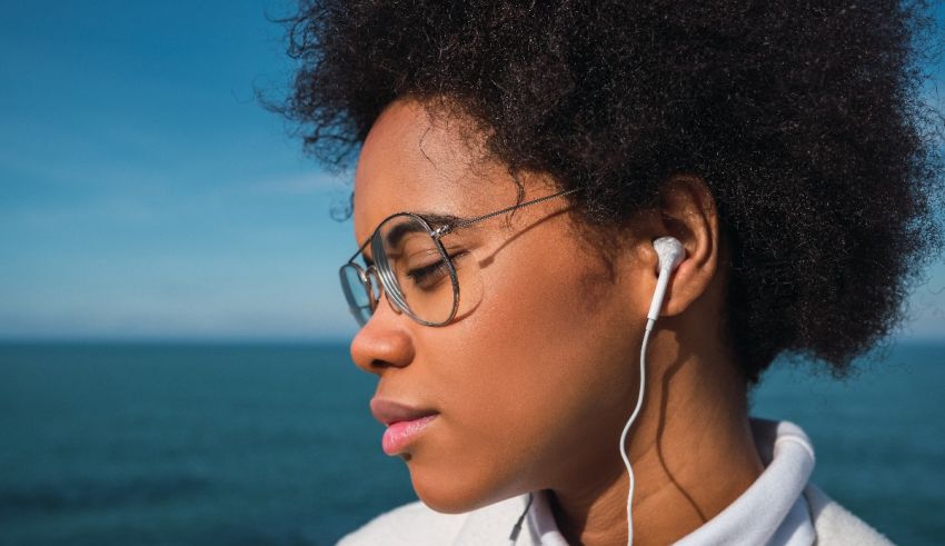 A woman wearing glasses and earphones near the ocean.