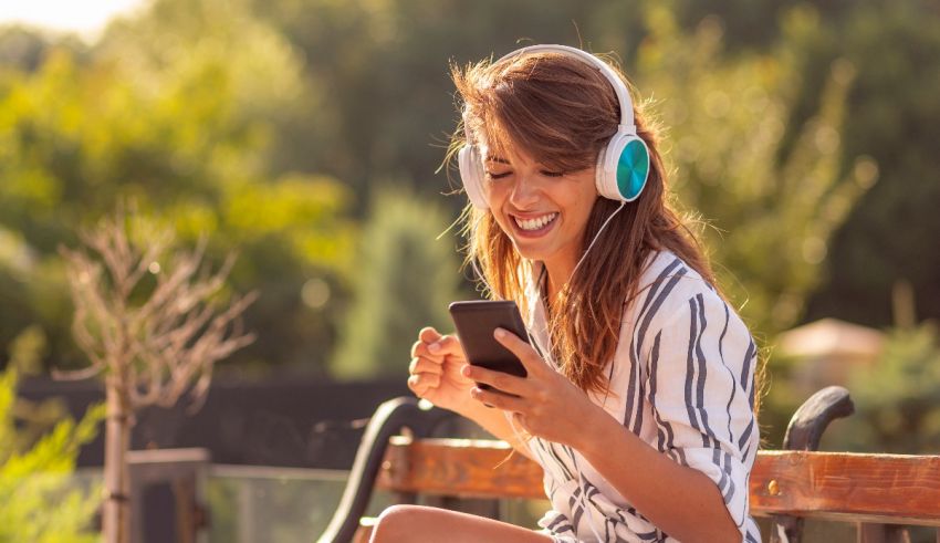 A woman is listening to music on her phone while sitting on a bench.