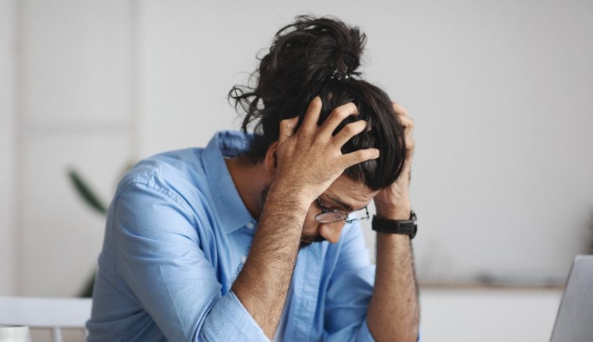 A man is sitting at his desk with his hands on his head.