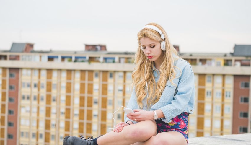 A young woman sitting on a ledge with headphones on.