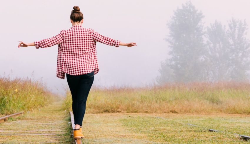 A woman is standing on a train track with her arms outstretched.