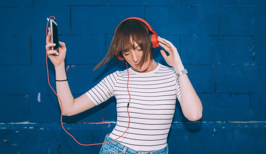 A young woman wearing headphones and listening to music on a blue wall.