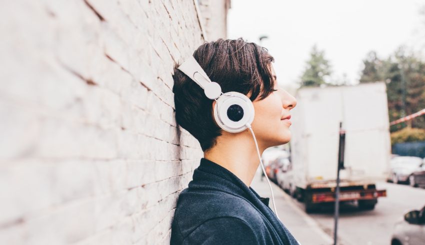 A young man wearing headphones leaning against a brick wall.