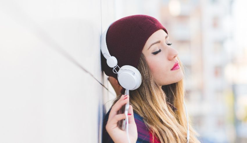 A woman wearing headphones leaning against a wall.
