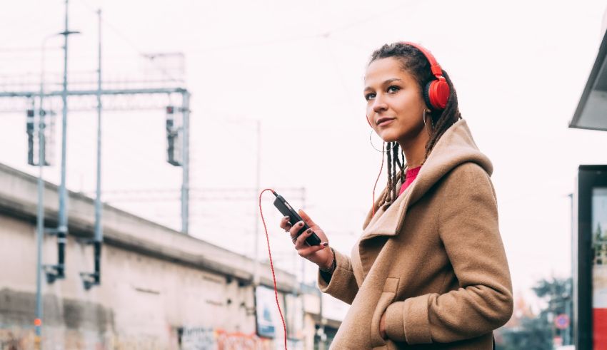 A woman wearing headphones is standing near a bus stop.