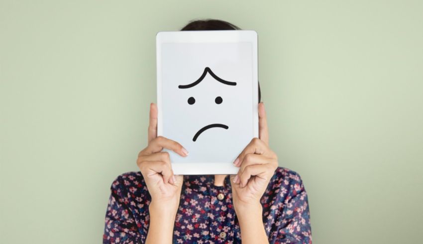 A woman holding up a tablet with a sad face on it.