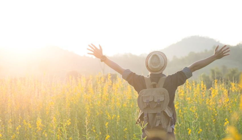 A man in a hat is standing in a field with his arms outstretched.