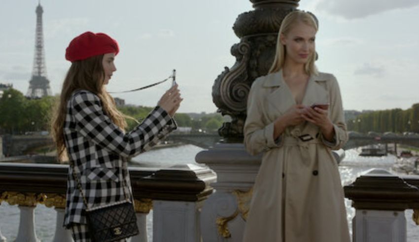 Two women standing on a bridge near the eiffel tower.