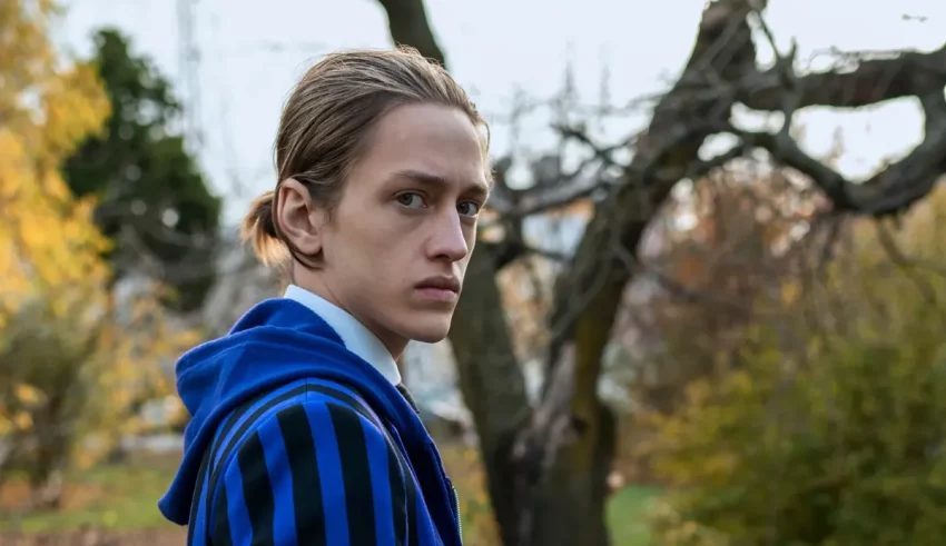 A young man in a blue striped jacket standing in a park.