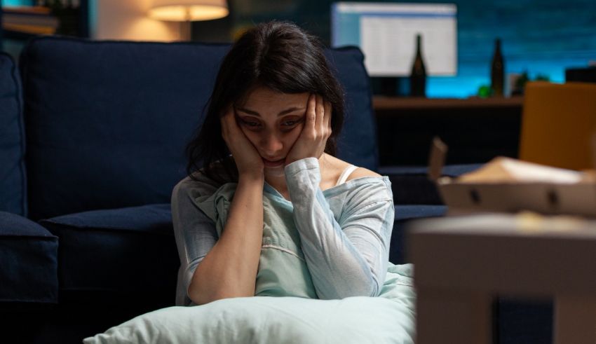 A woman is sitting on a couch with her hands on her head.