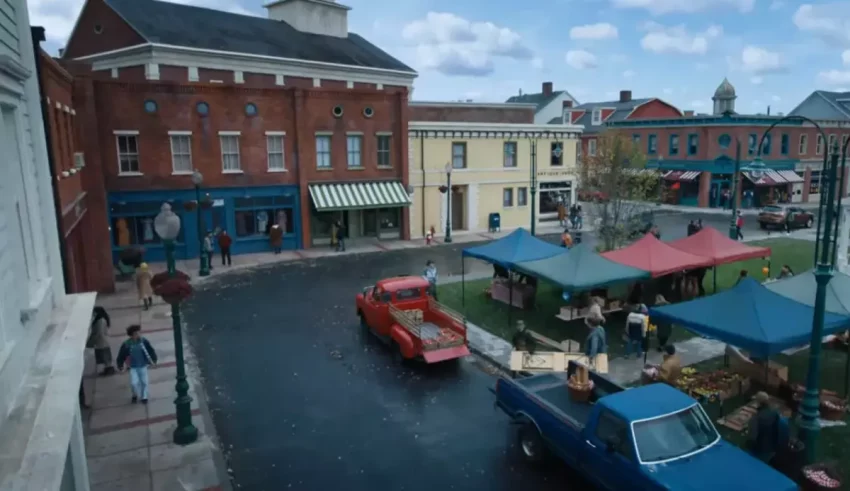 A blue truck is parked in front of a small town.