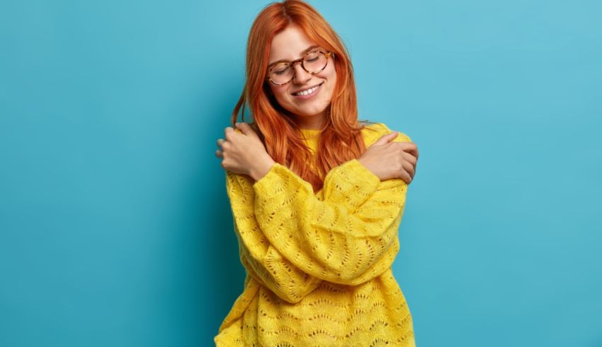 A young woman with red hair and glasses is posing against a blue background.