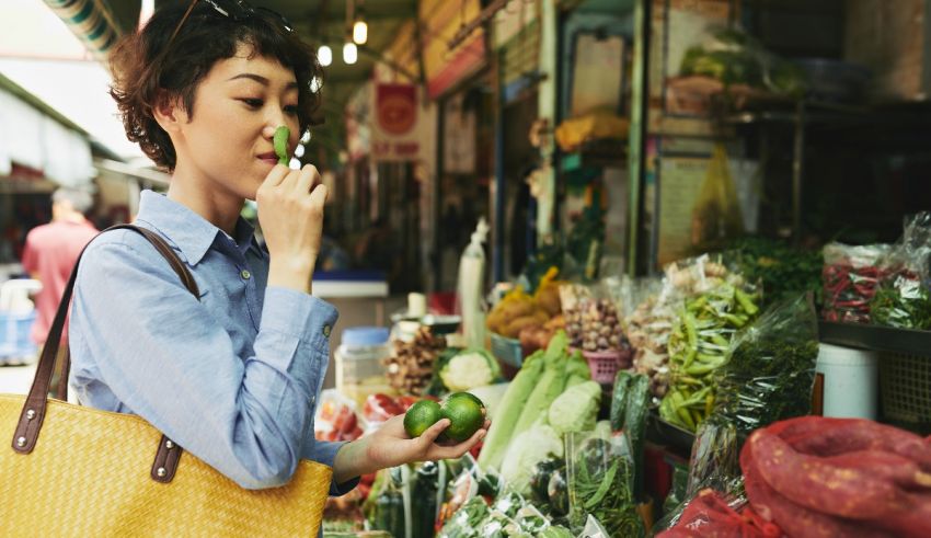 A woman is standing in front of a market full of fruits and vegetables.