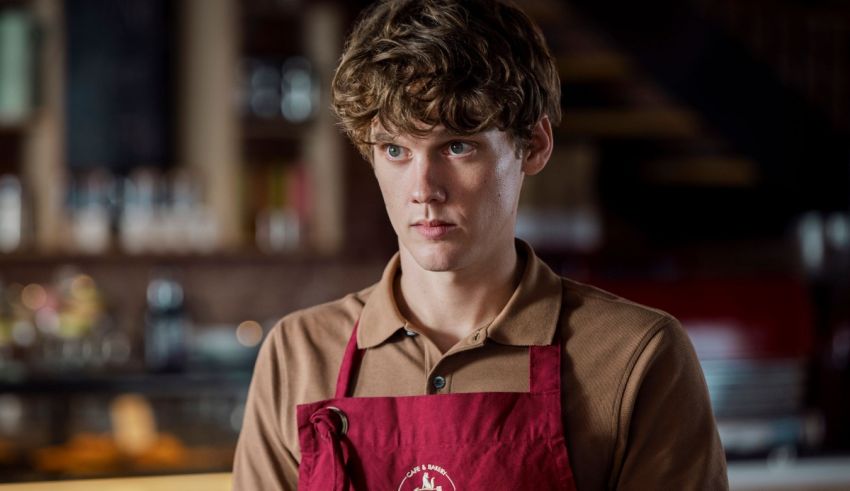 A young man in a red apron standing in a bar.